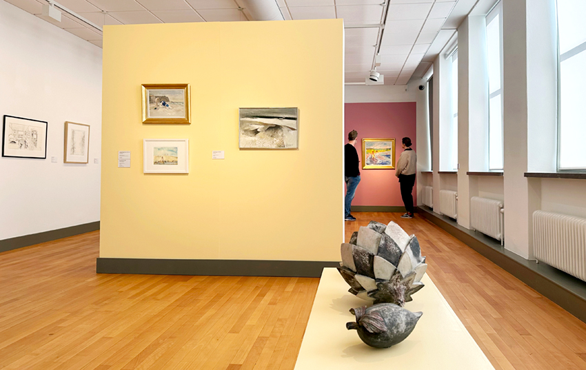 Utställningssal med skulpturer i förgrunden och tavlor i bakgrunden.