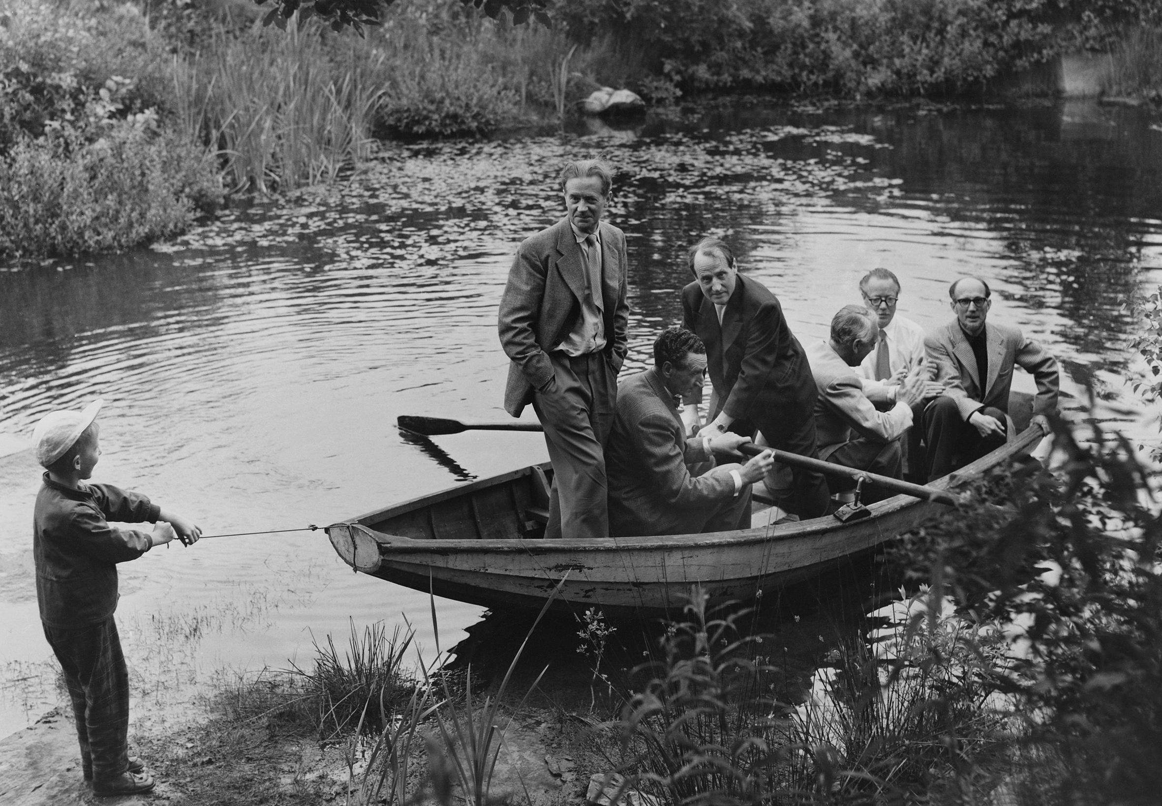 Gammalt svartvitt fotografi med sex män i en eka och en liten pojke som håller på att dra iland ekan.