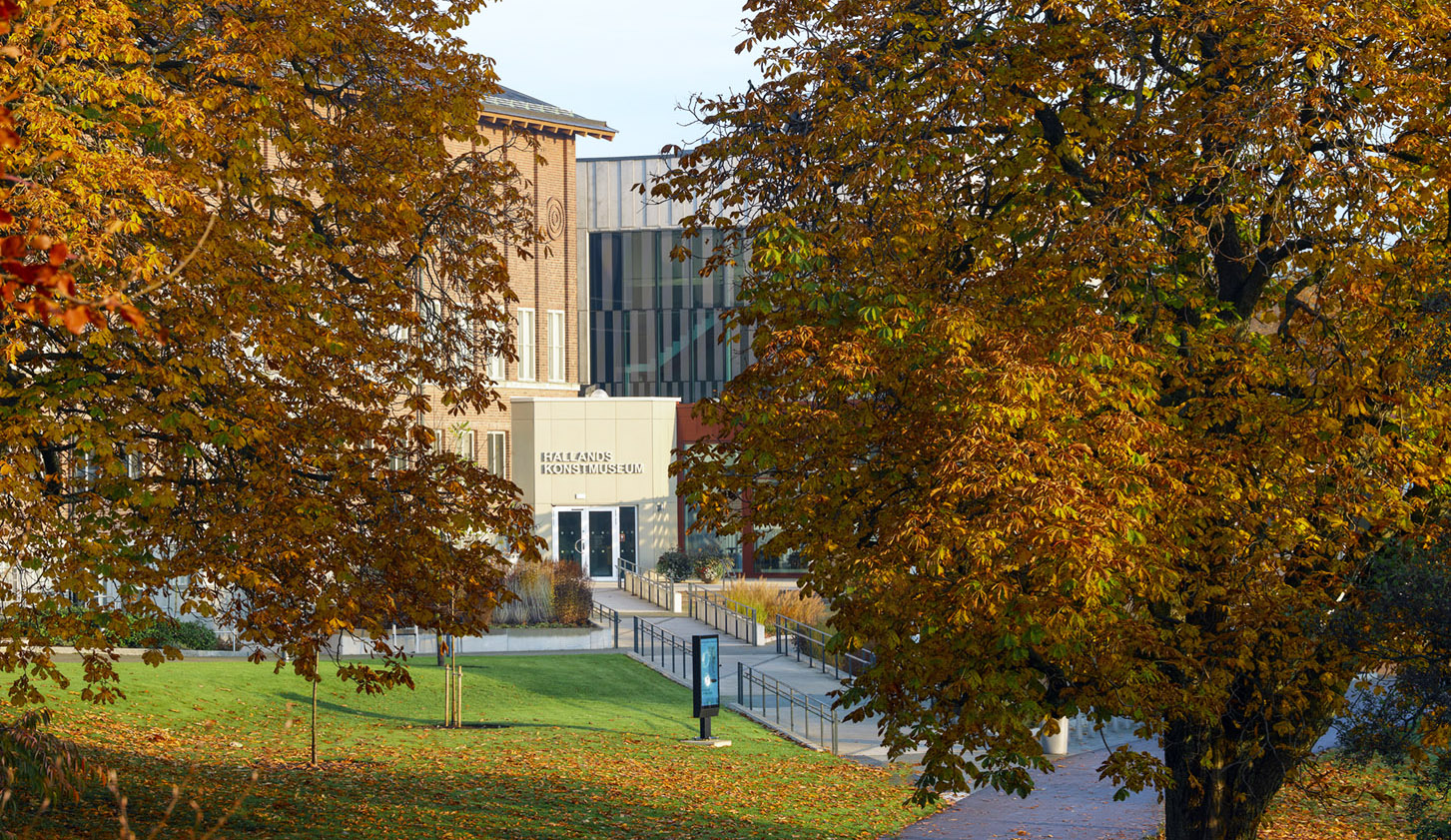 Entrén till Hallands Konstmuseum skymtar bakom stora träd med höstlöv.