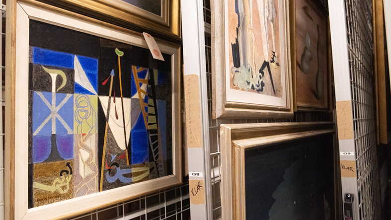Närbild på tavlor som hänger på gallergrindar i Hallands Konstmuseums konstmagasin.