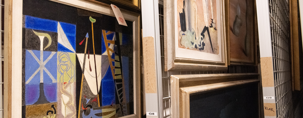 Närbild på tavlor som hänger på gallergrindar i Hallands Konstmuseums konstmagasin.