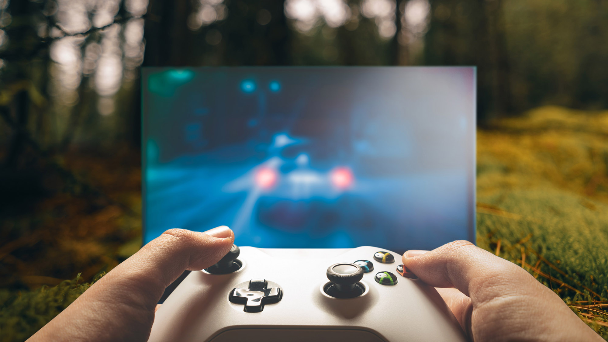 Händer som håller i spelkonsol i en skog.