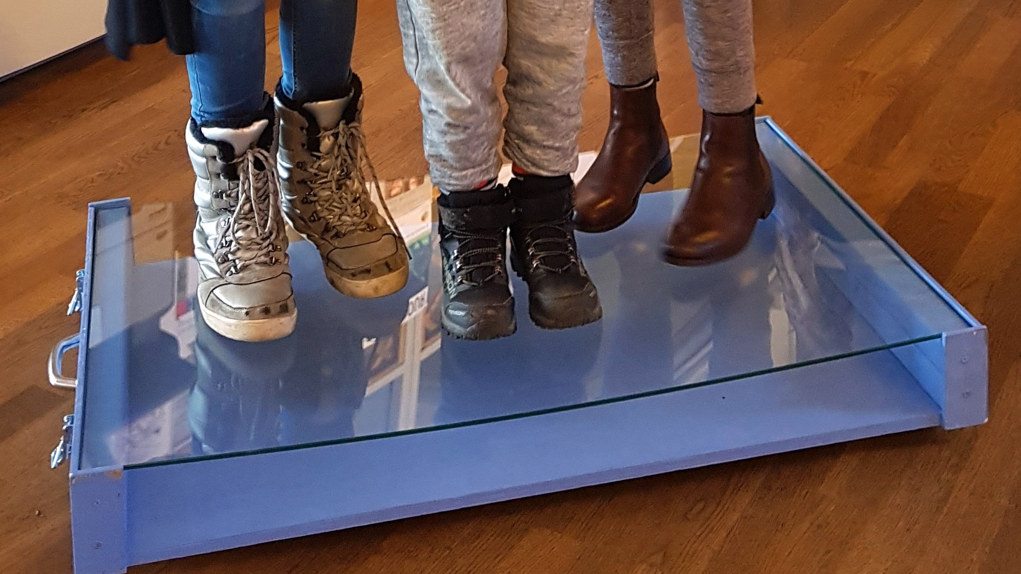 Tre par fötter som står på en glasskiva.